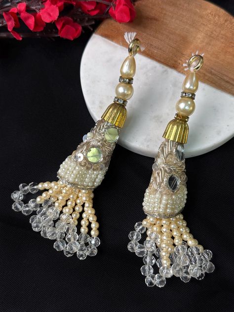 ➤The latkans feature multiple strings adorned with lustrous creme pearls and sparkling crystal beads. The combination of pearls and crystals creates a mesmerizing play of light and texture, making these tassels a captivating focal point of any outfit. ➤Versatile and easy to attach, these latkans can be effortlessly added to the ends of your blouse, dupatta, lehenga, or sari pallu, or even used as waist belt tassels. They provide a graceful movement and a touch of glamour, elevating your ensemble to a whole new level of opulence. ➤Product Details: - Materials: Pearls, crystal beads, thread - Color: Off White - Design: Multi-string hanging latkan with pearls and crystals - Usage: Perfect for bridal Indian blouses, dupattas, lehengas, saris, and waist belts - Quantity: Pair of 2 latkans - Att Pearl Tassels, Indian Blouses, Waist Belts, Indian Blouse, Indian Lehenga, Sparkling Crystal, White Design, Waist Belt, Crystal Beads