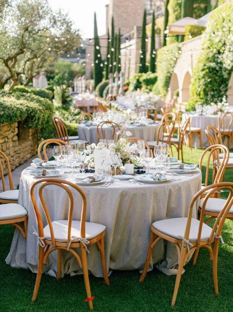 Elegant round table setting with pastel floral arrangements, vintage chairs, a white table spread, and hanging lights at a Provence wedding reception. Provencal Wedding Theme, French Country Wedding Theme, Airelles Gordes, Pastel Floral Arrangements, French Wedding Decor, Light Wood Chairs, Table Spread, French Country Wedding, Chinese Heritage