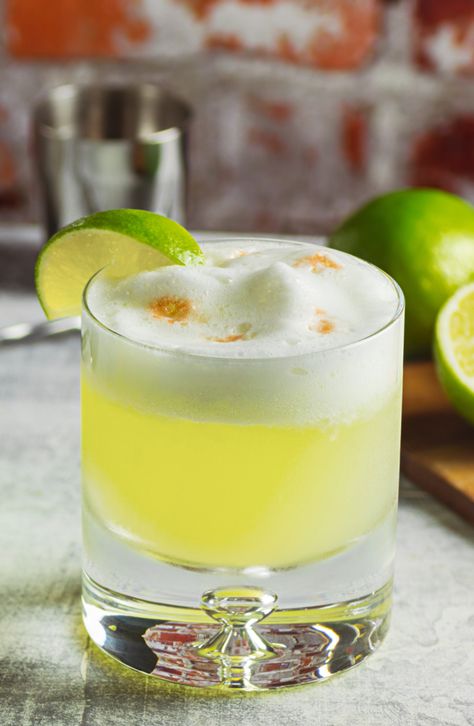 A round cocktail glass is filled with bright green liquid and topped with foamy egg whites. A lime wedge rests on the side of the glass. Pisco Drinks, Pisco Cocktails, Pisco Sour Recipe, Sour Cocktails, Sour Drink, Strong Cocktails, Sour Foods, White Cocktails, Pisco Sour