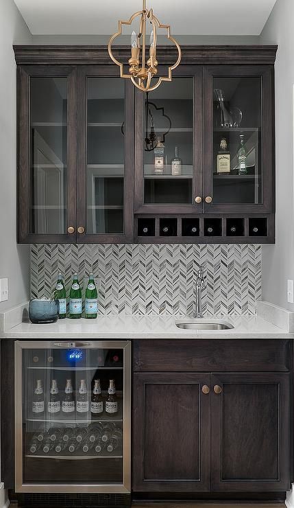 Exquisite brown wet bar boasts dark brown shaker cabinets accented with brass nobs and fitted in a nook beside a glass front beverage fridge located under a white quartz countertop. Small Home Bar Ideas, Small Bars For Home, Bar Nook, Shaker Kitchen Cabinets, Small Bars, Built In Bar, Home Bar Designs, Cocktails Bar, Shaker Cabinets