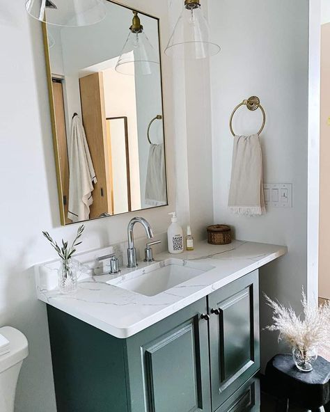 Blue green bathroom vanity is complete with a white quartz countertop and chrome faucet. Vintage glass vanity lighting is displayed above a rectangular brass framed mirror. Brass towel ring is affixed beside the vanity and hosts a beige hand towel. Green Bathroom Vanity Ideas, Green Blue Bathroom, White Herringbone Tile Floor, Blue Green Bathroom, Brass Framed Mirror, Marble Countertops Bathroom, Brass Towel Ring, Blue Green Bathrooms, Bathroom Inspo Interior Design