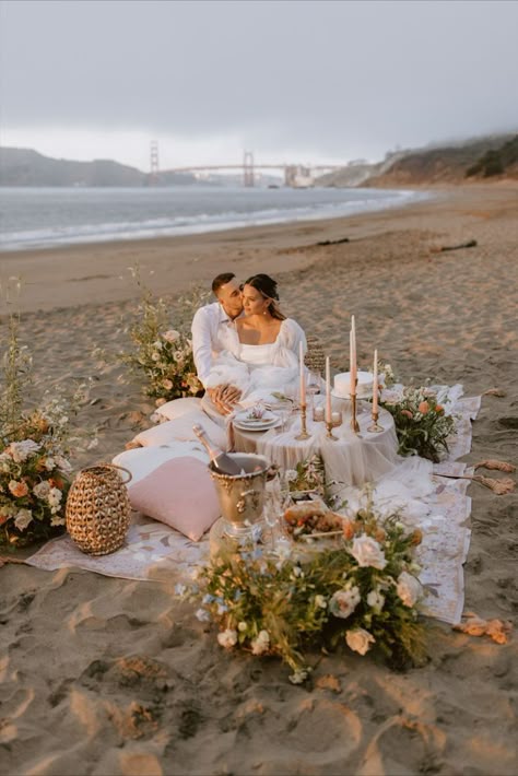 Bride and groom sitting at beach picnic with beautiful flowers and pink decorations at sunset Proposal Ideas Beach, Boho Beach Elopement, Wedding Proposal Ideas Engagement, Romantic Beach Picnic, Elopement Picnic, Cute Proposal Ideas, Wedding Proposal Ideas, Picnic Engagement, Dream Proposal