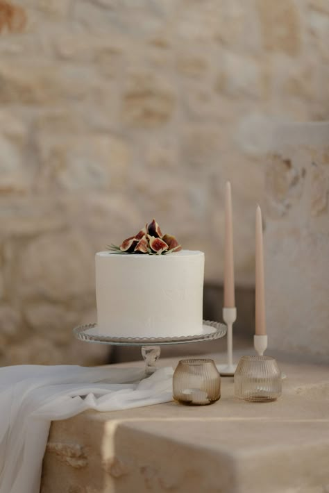 Simple iced wedding cake with figs and blush tapered candles at private villa wedding in Greece Italian Inspired Wedding Cake, Stenciled Wedding Cakes, Mediterranean Wedding Cake, Italy Wedding Cake, Bare Cake Wedding, Fig Wedding Decor, Italian Wedding Desserts, Fig Wedding Cake, White Simple Wedding Cake