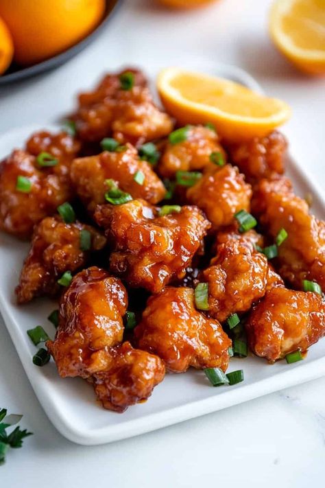 Slow Cooker Orange Chicken. A plate of crispy orange chicken bites, glazed with a sticky orange sauce, garnished with fresh scallions. A wedge of fresh orange sits in the background, adding a burst of color. Slow Cooker Orange Chicken Recipes, Orange Chicken Crockpot Recipes, Crockpot Orange Chicken Recipe Easy, Orange Chicken Recipe Crockpot, Orange Chicken Crockpot, Asian Banquet, Crockpot Orange Chicken Recipe, Weekend Dinner Ideas, Saturday Night Dinner Ideas