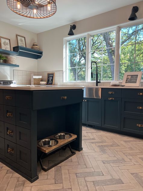 This kitchen is the ultimate inspiration for any dog lover out there! The center island has a built-in nook specifically designated for a dog food and water dish! It blends in seamlessly to the dark cabinetry and the herringbone floor adds so much character to this space!   New Construction | Home Trends 2024 | Home Design | Minnesota Home Trends Dog Bowl Station Kitchen Island, Dog Food In Island, Dog Crate Island Kitchens, Kitchen Dog Bowls Built Ins, Dog Dish In Island, Dog Bowl Kitchen Island, Dog Bowls In Island, Island With Dog Bowls Built Ins, Kitchen Island Dog Bowl