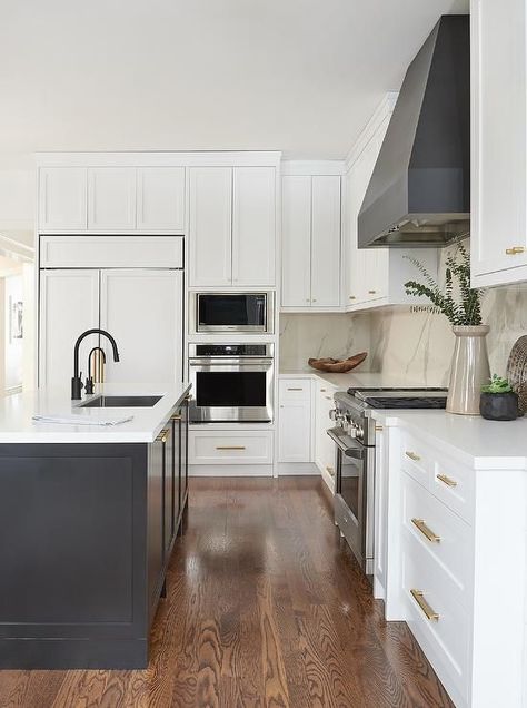 Contrasted with white shaker cabinets donning brass hardware, a black hood is fixed to a marble-like quartz slab backsplash over a stainless steel oven range. Dark Blue Kitchen Cabinets, Top Kitchen Cabinets, Modern Kitchen Renovation, Minimal Kitchen, Blue Kitchen Cabinets, White Shaker Cabinets, Kitchen Hoods, Shaker Cabinets, Transitional Kitchen