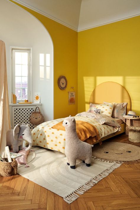 A kids’ room in warm yellow hues. The bed is dressed in kids bed linen with a sun print. By the end of the bed, there’s a soft, white rug placed on the floor. A giant alpaca soft toy is standning next to the bed. Bedroom Inspirations Yellow, Yellow Kids Bedroom, Yellow Kids Rooms, Small Baby Room, Minimalist Kids Room, Kids Bed Linen, Cool Kids Bedrooms, Childrens Bedroom Decor, Hm Home