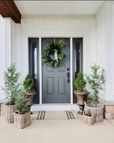 A black door with white front door trim is paired with black sidelights. Pine trees in wicker planters are arranged in front of the door on this porch with a beige and black striped doormat...   Image: fiveacresonbrook White Lantern Decor, Christmas Front Porch Decor Ideas, Christmas Front Porch Decor, White Front Door, Front Door Trim, Front Porch Decor Ideas, Holiday Living Room, Christmas Color Palette, Front Door Christmas Decorations