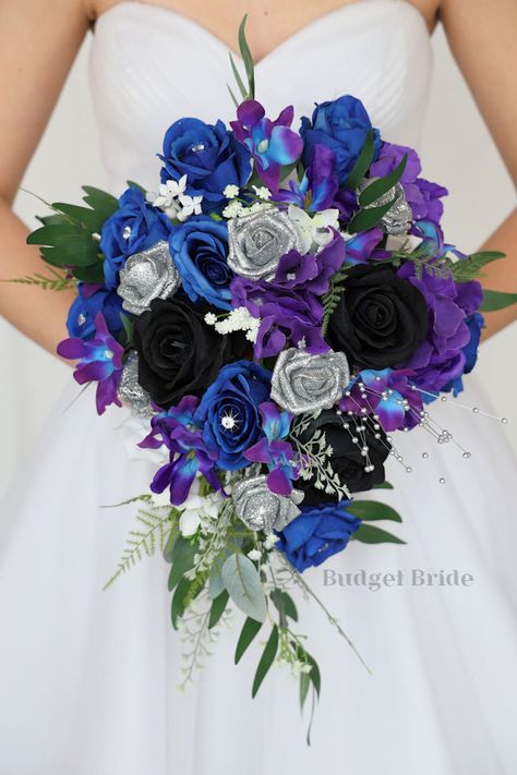 This lovely assortment of royal blue, purple and black roses is bound to turn heads on your wedding day. This lovely cascading brides’ bouquet from the is an absolutely breathtaking arrangement for any bride to be, in any season. Galaxy orchids and silver accents complete the look and add a delicate realism to this beautiful bouquet. This bouquet is 10” wide, 18” long, and is crafted by our in-house florists without using a foam base to anchor the flowers to the bouquet. Instead, we wire our bou Violet And Blue Wedding Theme, Purple Teal Silver Wedding, Black Blue And Purple Wedding Dress, Royal Blue And Plum Wedding Theme, Royal Blue Purple And Silver Wedding, Purple Blue Black Wedding, Dark Blue And Dark Purple Wedding, Galaxy Flower Arrangement, Purple And Blue Flowers Wedding