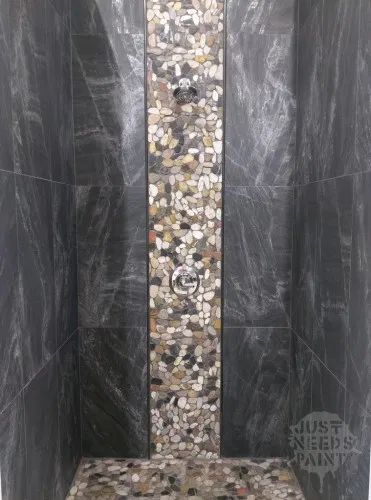 Mixed medium brown flat pebble mosaic on a shower wall. The separate mosaic 12" "tiles" are hard to see with only a single column. Shower With Rock Floor Pebble Tiles, Slate Shower With Pebble Floor, Rock Shower Ideas, Master Shower Tile Pebble Floor, Pebble Stone Shower Floor Dark, Black And Gray Pebble Shower Floor, Pebble Shower, River Rock Shower, Rock Shower