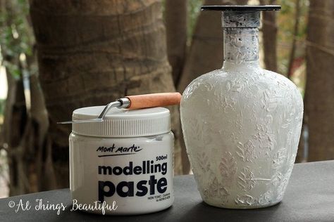 Altered Bottle Art is a great idea for wedding centerpieces and home decor. Here is a step by step tutorial to re purpose bottles to create a lovely centerpiece. Step 1: Start with applying a coat of gesso onto a clean bottle and let dry. Step 2: Use a stencil and apply modelling paste to add texture to the surface of the  bottle. Let dry for a few hours. Step 3: Apply a coat of chalk paint and let the paint dry. I have dabbed the chalk paint using a paint brush to add textu… Altered Bottles Tutorial, Reuse Wine Bottles, Altered Jars, Re Purpose, Idea For Wedding, Clean Bottle, Decoupage Glass, Glass Bottle Diy, Modeling Paste