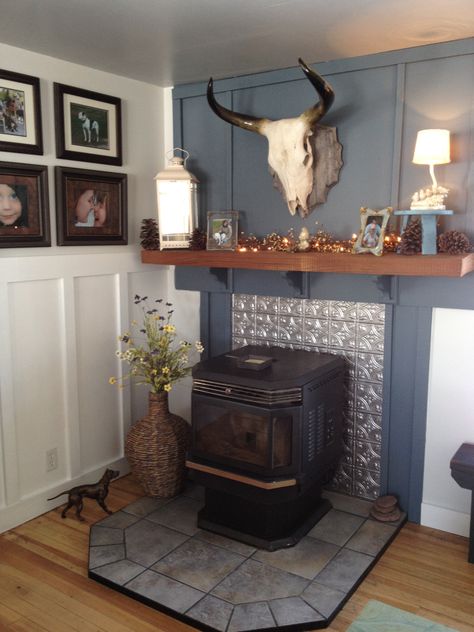 Turn a hulking pellet stove into a charming fireplace simply by adding tin tiles behind it.  Firring strips nailed over sheet rock and a slab of rough cut oak create a mantle.  Benjamin Moore Province Blue - fireplace, Benjamin Moore Horizen - Upper wall, Behr Ultra Pure White - Board and Batten, Benjamin Moore Pale Smoke - ceiling Stove Surround Ideas, Living Room Wood Stove, Wall Behind Stove, Pellet Stove Hearth, Stove Surround, Corner Wood Stove, Wood Stove Surround, Stove Hearth, Corner Stove