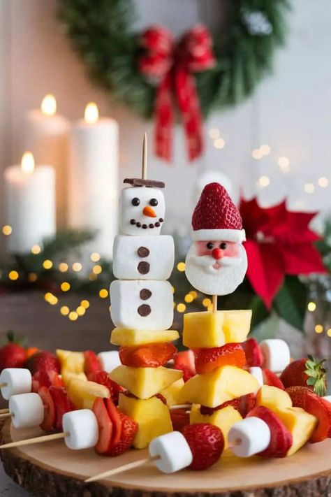 Festive fruit and marshmallow skewers shaped like a snowman and Santa, with holiday decorations in the background. Santa Fruit Kabobs, Christmas Fruit Kabobs, Snack Low Calorie, Christmas Family Dinner, Strawberry Santa, Santa Treats, Snack At Home, Strawberry Santas, Low Calorie Recipe