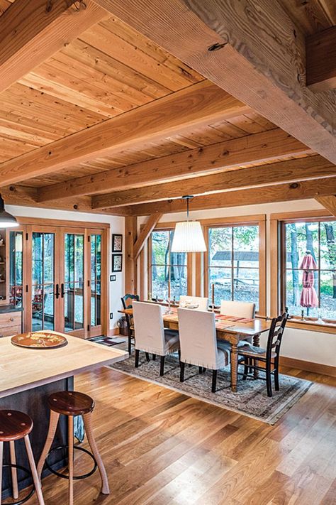 The connected open space on the 1,200 square-foot main level is filled with dining, living and kitchen areas. The Douglas fir posts and timbered ceilings establish a sense of contentment and comfort, while the abundant natural light gives it levity and space to breathe. The kitchen’s perimeter counters are capped with Corian while the center island is topped with silky maple. Photography by Scott Hemenway. Douglas Fir Walls, Timber Frame House Interior, Douglas Fir Ceiling, Timber Ceilings Interior, Timber Frame Interior Design, Timber Frame Home Interiors, Barndo Interior, Timber Frame Interior, Timber Interior