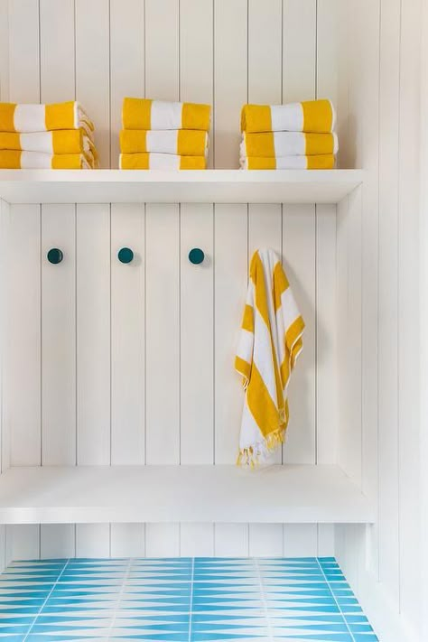 White and blue turquoise tiles lead to a white built-in bench fixed against vertical shiplap trim beneath peacock blue towel hooks. Poolhouse Bathroom, Chevron Floor Tile, Pool Pavillion, Pool Changing Room, Shiplap Trim, Art Curation, Pool House Cabana, Chango & Co, Pool House Bathroom