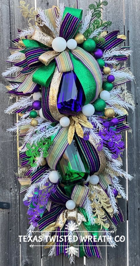 Set the mood for your Mardi Gras celebrations with this exquisite XL swag wreath! Bursting with vibrant designer ribbon, dazzling ornaments, sparkling jewels, and lush greenery, this wreath is a statement piece for your festive decor. Handcrafted with attention to detail, it's perfect for adding a touch of carnival flair to your home. Embrace the spirit of Mardi Gras in style with this opulent wreath! Built on an evergreen base. Measures 40 by 20 inches and is ready to ship.  Handmade in the USA Mardi Gras Swag, Bridal Show Booths, Peacock Christmas Tree, Mardi Gras Party Decorations, Peacock Christmas, Mardi Gras Wreath, Jeweled Christmas, Swag Wreath, Mardi Gras Decorations