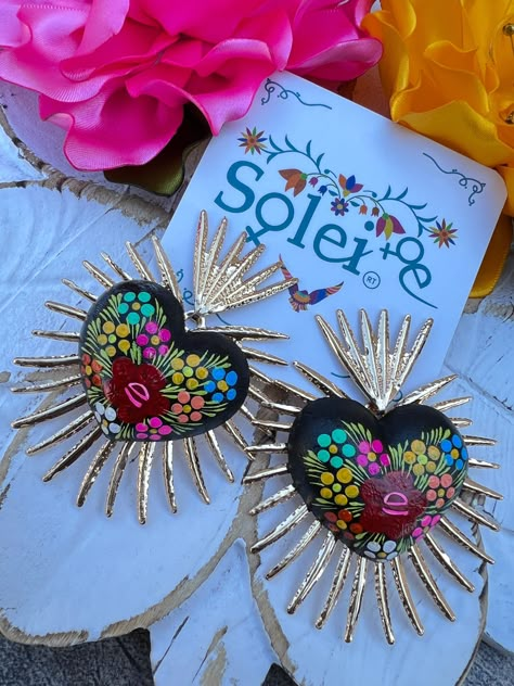 Infuse your style with a dash of Mexican charm with our hand-painted heart earrings. Each pair is meticulously crafted by skilled artisans, capturing the essence of Mexico's rich culture and artistic heritage.  Every piece is completely unique because of the detailed process that goes into creating it. The black lacquer is created by mixing in layers of dirt with a grease from the Cochinilla bug. The flowers are painted on with our finger tips using ground up natural pigments and linseed oil. To Mexican Heart Necklace, Dia De Los Muertos Decorations Ideas, Mexican Earrings, Mexican Crafts, Natural Pigments, Painted Hearts, Mexican Jewelry, Finger Tips, Painted Earrings