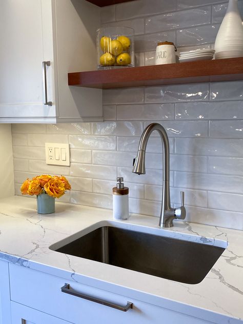 The subway tile backsplash adds texture and interest with a wavy, delicately textured surface, and a hint of color to provide a perfect backdrop for the white cabinets and maple floating shelves. Simple Grey Backsplash, White Textured Subway Tile Bathroom, Wavy Kitchen Backsplash, White Marble Subway Tile Backsplash, Backsplash For White Cabinets Subway Tile, Uneven Subway Tile Backsplash, White Wave Tile Kitchen Backsplash, White Tile Backsplash With White Cabinets, Wavy Tile Backsplash Kitchen