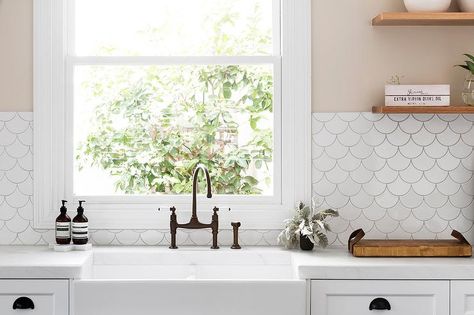 Cream kitchen walls accented with Tabarka Studio Artisan Terracotta Fan Tiles frame a window positioned above a farmhouse sink finished with a bronze faucet fixed to a honed white marble countertop located under stacked floating wooden shelves and complementing white shaker cabinets donning oil rubbed bronze cup pulls. Cream Kitchen Walls, Fish Scale Tile Backsplash, White Fish Scale Tile, Kitchen Wall Tiles Backsplash, Kitchen Wall Design, Scale Tile, Redo Kitchen Cabinets, Trendy Farmhouse Kitchen, Trendy Kitchen Tile