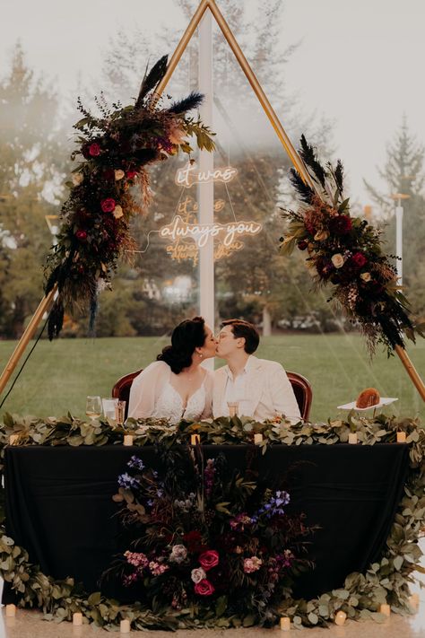 Two women, one in a white wedding dress and one in a white suit, sit under an arch kissing at the head table. Hanging from the arch and above them is a neon sign that reads “it was always you”. Flowers and LED candles surround them and the table. Moody Lesbian Wedding, Lesbian Halloween Wedding, Witchy Lesbian Wedding, Wlw Wedding Ideas, Wlw Wedding Aesthetic, Chaotic Trio, Wlw Wedding, Relationship Vision Board, Victorian Witch