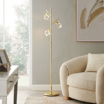 This 3-light floor lamp provides a mixture of modern and glam styles to elevate your living room arrangement. Crafted from steel with a shiny gold finish, it features a circular base and a tree-style silhouette with branches that angle out toward three corresponding fixtures. Each one holds an included LED bulb and is surrounded by a clear, multifaceted crystal glass shade. Measuring 5.5' tall and just under a foot wide, this lamp's small footprint makes it ideal for space-conscious rooms. Highl Living Room Arrangement, Room Arrangement, Light Tree, Crystal Floor, Crystal Floor Lamp, Ornament Stand, Tree Floor Lamp, Living Room Arrangements, Gold Floor Lamp