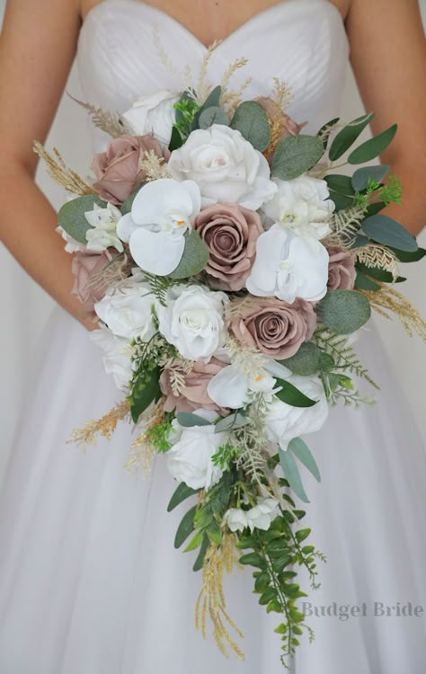 This lovely assortment of white and mauve roses is bound to turn heads on your wedding day. This lovely cascading brides’ bouquet from the is an absolutely breathtaking arrangement for any bride to be, in any season. Bright greenery, pampas grass and white orchids complete the look and add a delicate realism to this beautiful bouquet. This bouquet is 10” wide, 18” long, and is crafted by our in-house florists without using a foam base to anchor the flowers to the bouquet. Instead, we wire our bo Wedding Flower Bouquets Bridal Budget-bride.shop, Wedding Bouquet Neutral Colors, Succulent Wedding Flowers, Wedding Floral Bouquet Brides, Elegant Bridal Flowers, Bride’s Bouquet, Wedding Bouquet Beach, Wedding Bouquets Real Flowers, Bouquet Styles Shape