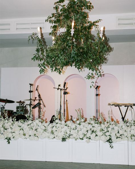 Let’s talk repurposing flowers from ceremony to reception. When those two events are in the same location, and there’s enough time for that transition to happen, and you have the approval of the full vendor team, it IS possible! For this wedding, a New Orleans second line distracted our guests while the huge chuppah broke down to lay across the fireplace mantle, and the aisle florals transitioned to stage front florals to hide the band equipment! The team had a plan, all hands were on deck, a... Band Backdrop Wedding, Band Backdrop, New Orleans Second Line, Aisle Florals, Party Location, Nola Wedding, Bar Fronts, Wood Tables, New Orleans Wedding