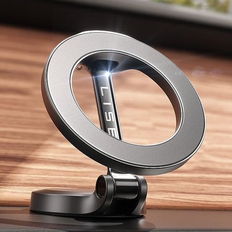 The photo shows a silver, steel alloy circular phone mount that uses MagSafe technology to hold the device in place.  It shows the mount set up on a flat surface with a wood panel behind it. Iphone Car Holder, Car Cell Phone Holder, Magnetic Phone Holder, Latest Iphone, Support Telephone, Car Holder, Phone Mount, Cell Phone Holder, Car Phone Holder