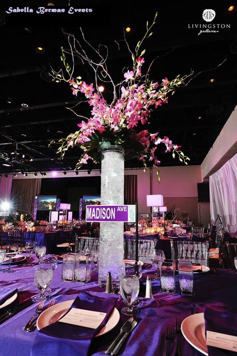 Sabella Berman Events used tall orchid centerpieces on the four corners of the ballroom in a NY themed party to define the space. In the vase we used purple LEDs, crinkle cello and water to give a crushed ice effect. Two other centerpieces were used on a collection of over 16 tables. Each unique, with a NY themed street name on mini tabletop lampposts. New York Theme Quinceanera, New York Fashion Week Themed Party, City Themed Centerpieces, New York Prom Theme Decoration, Ny Theme Party, Sweet 16 New York City Theme, New York Sweet 16 Theme, Nyc Sweet 16, Nyc Themed Party