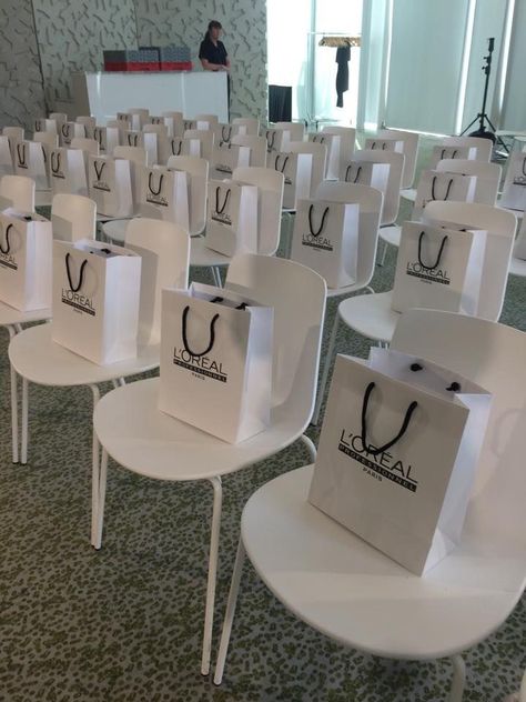 Simple and Minimalistic corporate event chair arrangement with souvenir bags Fashion Show Gift Bags Ideas, Grand Opening Goodie Bags, Event Goodie Bags, Beauty Masterclass Event, Makeup Event Ideas, Work Event Decor, Corporate Goodie Bags, Makeup Launch Party Ideas, Makeup Goodie Bags Ideas