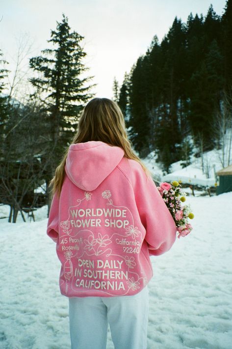 photo shows a blonde teenage girl standing in a snowy field. she is facing away from the camera and looking at the pine trees in the mountains in the distance. she is wearing white pants and a pink hoodie that says "worldwide flowers shop" "open daily in southern california" embroidered on the back in white. she is holding a bouquet of flowers in her hands, we can see the flowers resting on her arm. photo was taken on film Hoodie Wishlist, Aura Clothing, Dandy Worldwide, School Wishlist, Hoodie Outfits, Flower Hoodie, Wishlist 2024, Preppy Stuff, Preppy Clothes