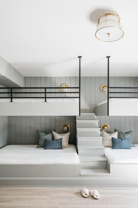 A pair of light gray bunk beds are separated by a light gray staircase, fixed against gray vertical plank trim, and accented with black railing lit by brass porthole sconces. Corner Bed Ideas, Grey Bunk Beds, Kate Marker Interiors, Modern Bunk Beds, White Bunk Beds, Bunk Beds Built In, Bed In Corner, Built In Bunks, Bunk Rooms