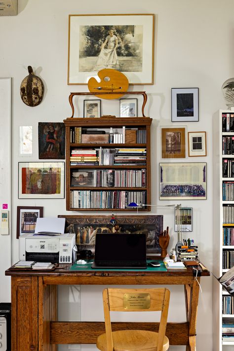 Step inside this Belfast studio to find an artist's eclectic work from home office. A vintage paint palette and fountain pen decorate the space above the desk. Below, a small bookshelf is filled to the brim with CDs. Assorted framed photos and drawings cover the walls, each with a different artistic style to create a unique gallery wall. The desk itself is made of rich wood, it is paired with a custom-engraved chair. Desk With Shelf Above, Living Room With Work Desk, Wall Desk With Shelves, Bookshelf Above Desk, Vintage Eclectic Home Decor Ideas, Graphic Designer Desk Setup, Writers Bedroom, Vintage Desk Aesthetic, Vintage Office Decor Ideas