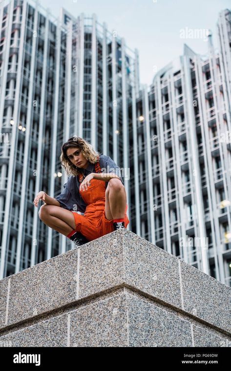 Download this stock image: Beautiful woman wearing dungarees, crouching on ledge in front of modern high-rise building - PG69DW from Alamy's library of millions of high resolution stock photos, illustrations and vectors. High Rise Building, Dynamic Poses, Image Processing, Dungarees, Beautiful Woman, Pose Reference, Print Images, Art Reference, Photo Image