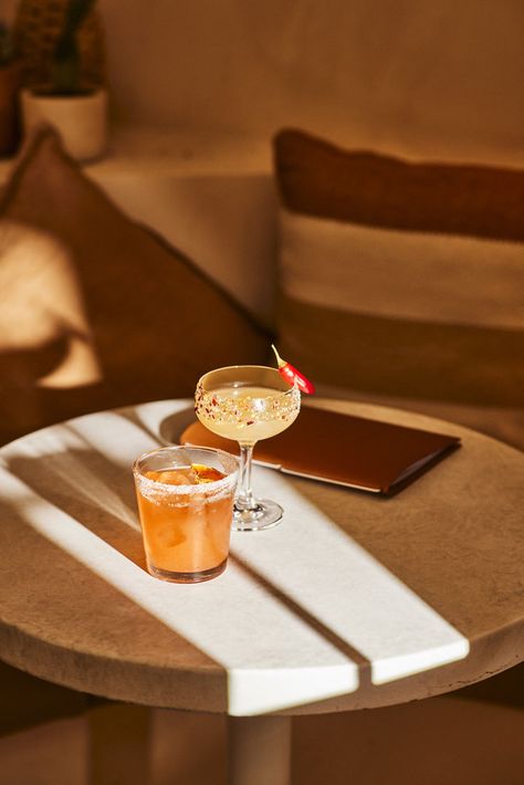 Cocktail photography of two margaritas upon a circular marble table in a Mexican themed bar. A short orange cocktail sits in a tumbler, with a salted rim. A chilli margarita in tall coup glass, decorated with salt, chilli flakes and a whole red chilli. Image belongs to Instant Crush Creative. Fun Cocktail Photography, Margarita Cocktail Photography, Cocktail Styling Photography, Spring Cocktail Photography, Restaurant Cocktail Photography, Cocktail Bar Content Ideas, Lifestyle Cocktail Photography, Summer Cocktails Aesthetic, Bar Content Ideas