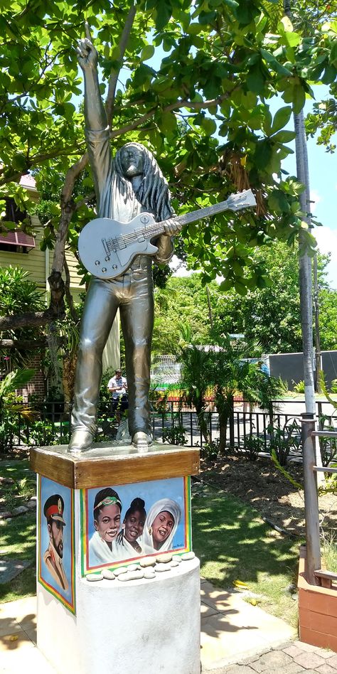 A life size silver statue of Bob Marley with clenched right hand in the air in a classic live performance pose. Bob has his Gibson guitar strapped on. The statue is on a wooden plinth, with paintings of the I Threes and Haile Salassie below the plinth. Bob Marley Museum, Blood Type Personality, Type Personality, Reggae Artists, Jamaican Music, Kingston Jamaica, Blood Type, West Indies, Bob Marley