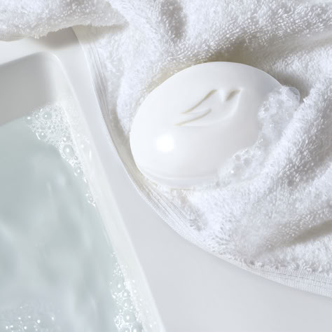 A white Dove Beauty Bar is covered in bubbles, and is sat on top of a white fluffy towel next to a white water-filled sink. Dove Soap Bar Aesthetic, Dove Soap Aesthetic, Bar Soap Aesthetic, Skin Care Icon, Dove Beauty Cream, Dove Bar Soap, Dove Bar, Dove Beauty Bar, Dove Soap