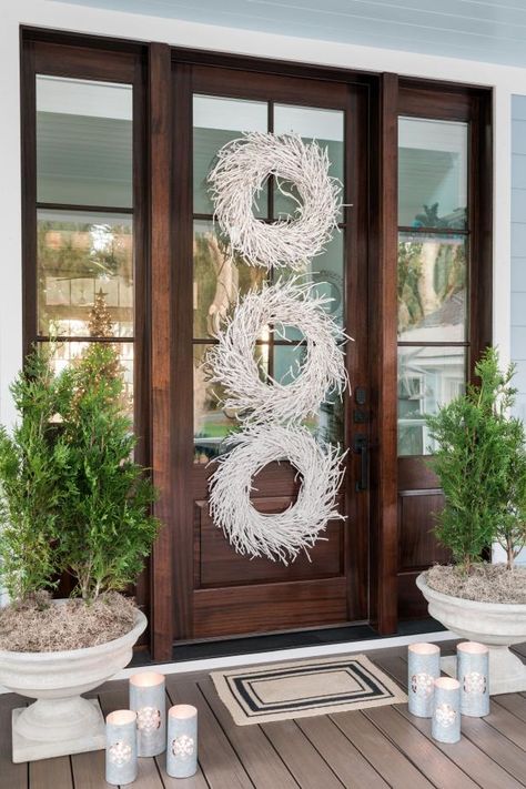 This coastal take on traditional front door decor creates depth and brings an element of whimsy. Mirroring the form of a jovial snowman, three vertically stacked driftwood wreaths combine for a big visual impact. Two petite evergreens on either side introduce vibrant color and round out the scene. Door For Christmas, Lake House Exterior, Holiday Door Decorations, Diy Christmas Door, Hgtv Dream Homes, Driftwood Wreath, Traditional Front Doors, Trees Lights, Christmas House Lights