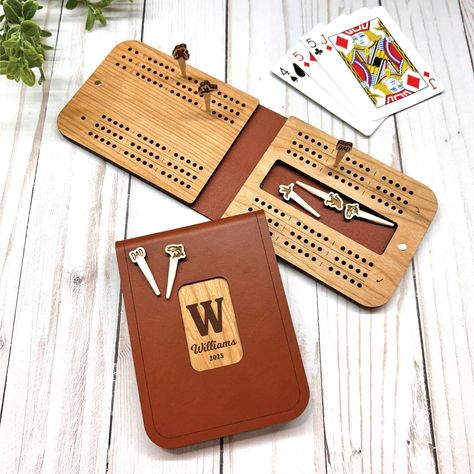 "Our new 3 track, 3 player travel cribbage board is the latest addition to our lineup of cribbage boards. Completely Custom Travel Cribbage Board inside and outside, with Custom Design Personalized Cribbage Pegs - Family Name Cribbage, Wildlife Cribbage, Unique Wedding Gift, Holiday Gifts, Travel and Camp Gifts! Our all natural leather and wood travel cribbage board is hand crafted from top to bottom and includes any 3 sets of our original personalized custom cribbage pegs! This game folds in ha Leather Cribbage Board, Unique Cribbage Board, Travel Cribbage Board, Camp Gifts, Cribbage Pegs, Custom Cribbage Board, Unique Window, Cnc Ideas, Laser Projects