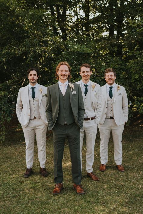 A groom stands with his groomsmen behind him. He wears a dark suit and they wear light neutral colour suits. Photography by Grace Elizabeth. Wedding Suits Groom Emerald Green, Sage Green Bride And Groom, Green And Cream Wedding Suits, Colored Grooms Suits, Green Suit Summer Wedding, Green Groom Suit With Groomsmen, Dark Sage Suit, Sage Green Wedding Suit Groomsmen, Pastel Wedding Groom Suit