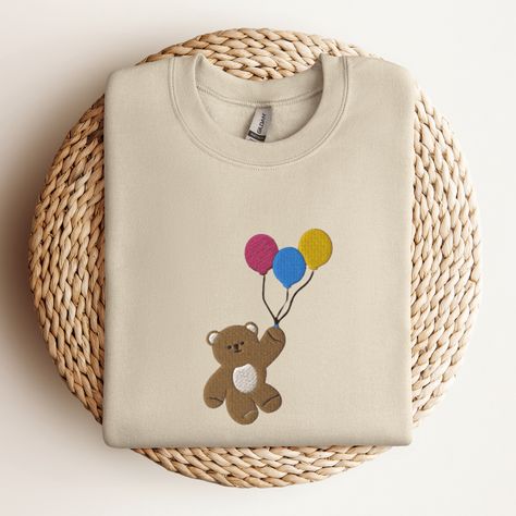 Cute Bear Sweatshirt, Bear with Balloons Embroidered Sweater, Embroidered Crewneck Sweatshirt, Funny Sweatshirt This embroidered bear crewneck sweatshirt is everything. Perfect to wear when you just want to fly away. Please let me know if you would like extended sizing (3X-5X), I have certain color and size options available! ✨ 50% cotton, 50% polyester ✨ Pre-shrunk ✨ Classic fit Care: Machine wash: warm (max 40C or 105F) Tumble dry: low Do not iron directly on the print Graphic Tee With Bear Design And Crew Neck, Cute Cotton T-shirt With Bear Design, Bear With Balloons, Embroidered Bear, Crew Neck T-shirt With Bear Print For Streetwear, Cute Bear Print Crew Neck T-shirt, White Crew Neck T-shirt With Bear Print, Bear Sweatshirt, Animal Sweater