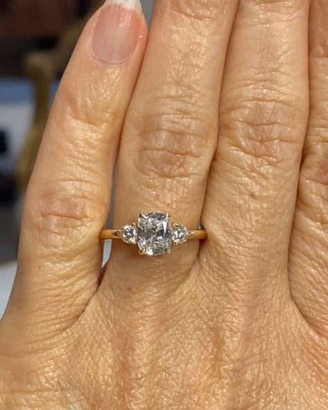 Cynthia Britt Custom Jewelry on Instagram: "A beautiful engagement ring for lovely Brenda! 🌟Story: Kathryn wanted a surprise engagement ring for Brenda. She had asked Brenda about her preferences so when time came, she asked her friends Scott and Kate, (I have created their engagement ring, wedding bands and a baby gift) for a recommendation and they referred me.  Kathryn knew Brenda liked an elongated cushion cut diamond preferably in a three stone ring. She was open to suggestions for both the center diamond and the style of the ring.  I first brought her a few diamonds to pick from and she chose an amazingly cut cushion brilliant cut diamond. Based on her chosen diamond and Brenda's hand structure and personal style, I recommended one round brilliant cut diamond on either side of the 3 Stone Elongated Cushion Engagement Ring, Unique Three Stone Engagement Rings, Elongated Cushion With Side Stones, Cushion Cut Three Stone Engagement Ring, Three Stone Cushion Engagement Rings, Elongated Cushion Three Stone, Three Diamond Engagement Rings, Hand Structure, Cushion Cut Engagement Ring Gold