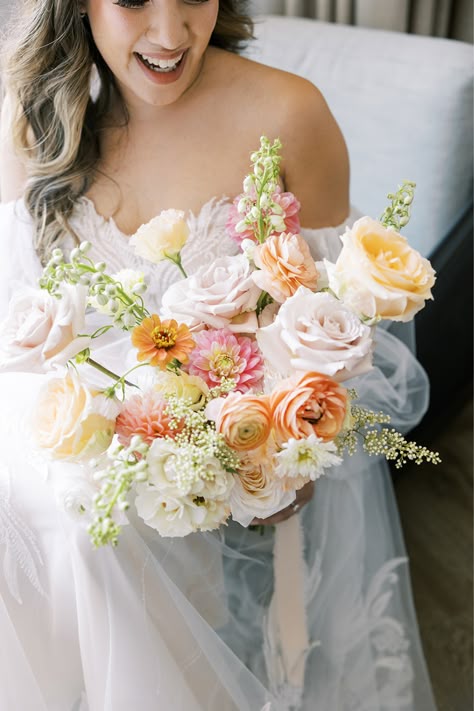 This romantic bridal bouquet was created for a bride and groom who got married this summer at Morgan's on Fulton. These soft, boho blooms were designed and provided by Romee Willow Florals, an artful and eco-friendly florist. Flowers used in this bouquet were blush ranunculus, light pink dahlias, peach roses, blush roses, white delphinium, orange zinnias, and more. We love this portrait of the bride and groom under the bride's veil! To see more photos by Rachael Kazmier, click the link. Floral Ceremony Backdrop, Dahlia Bridal Bouquet, Blush Ranunculus, White Delphinium, Pastel Bridal Bouquet, Yellow Bridal Bouquets, Orange Bridal Bouquet, Pink Dahlias, Garden Rose Bouquet