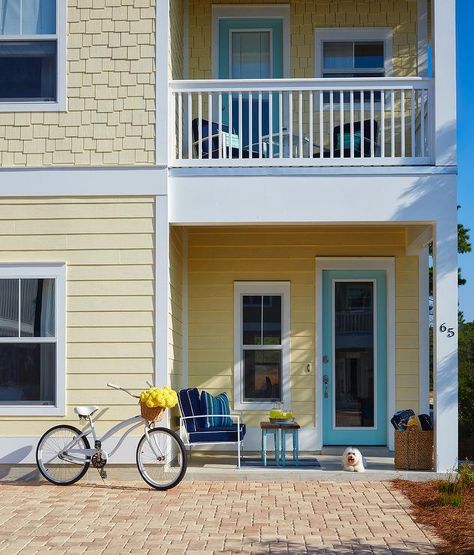 Side view of a yellow two story house with a turquoise blue front door under a second level balcony. Yellow Beach House, Yellow House Exterior, Paint Trim, Cream Kitchen, Beach House Exterior, Seaside Living, House Of Turquoise, Cottage Exterior, Yellow House