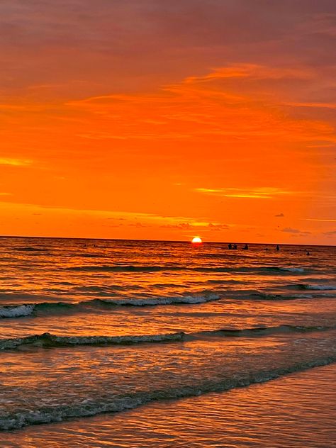 A view of the sunset at the shore from the beach. The sky is a bright orange with half of the sun still shining. Soft waves are flowing onto the shore. The waves have a bit of the orange reflected onto them from the sunset. Golden Hour At The Beach, Orange Ocean Aesthetic, Real Sunset Pictures, Orange Sunset Beach, Pretty Sunsets, Sunrise Orange, Ocean Surf, Orange Sunset, Sky Pictures