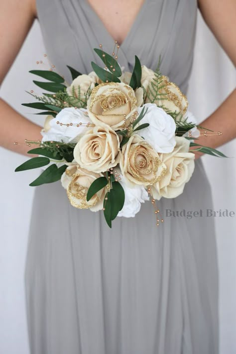 This lovely assortment of gold glitter tip, champagne and white roses and luxurious greenery is bound to turn heads on your wedding day. This lovely cascading brides’ bouquet from the Revy collection is an absolutely breathtaking arrangement for any bride to be, in any season. Gold leaves and gold pearls complete the look and add a delicate realism to this beautiful bouquet. This bouquet is 10” wide, 18” long, and is crafted by our in-house florists without using a foam base to anchor the flower Bouquets For Weddings Brides, Bridal Bouquet White And Champagne, Champagne Gold Flowers, Cream And Gold Bouquet, Sage And Gold Bouquet, Green And Champagne Wedding Flowers, Gold And White Wedding Bouquet, Sage Green And Gold Bouquet, Emerald Green And Champagne Wedding Bouquet