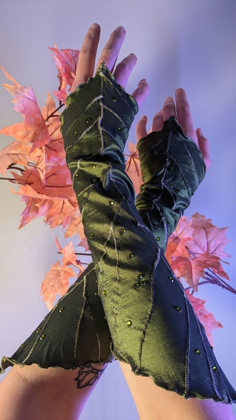 Wearable leaves! Don these deluxe leaf gauntlets to elevate your LARP, Ren Faire, or fantasy costume. Made out of a polyester/spandex stretch taffeta in Spring or Forest green, with extra embroidery details and glass rhinestones for some dewy sparkle. Approx. 15 inches long from tip to tip. Mystery drawstring storage bag included with every leafy order! Looking for a different color? Contact me for a custom listing! Long & Short Leaf Gauntlets are also available in the shop! Fantasy Leaf Shoes, Layered Ren Faire Outfit, Forest Themed Costume, Fallen Fairy Costume, Green Fairy Ren Faire, Clothes Made Of Leaves, Green Mushroom Hat, Nature Elf Outfit, Dnd Clothes Ideas