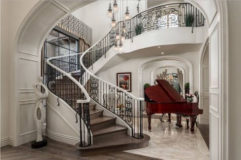 Elegant entryway with contemporary sculpture and baby grand piano along with a wooden staircase fitted with ornate wrought iron railings and illuminated by glass globe chandelier. French Provincial Home, Staircase Styles, Lux Home, Modern Mediterranean Homes, Luxury Staircase, Rooftop Dining, French Villa, Glamour Decor, City Homes