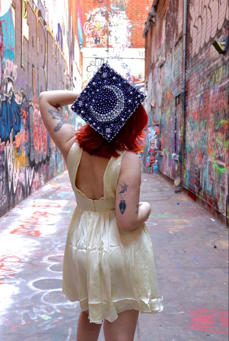 College senior graduation photo with beaded celestial graduation cap design inside alley filled with graffiti Stars Graduation Cap, Gad Cap Ideas, Angel Graduation Cap, Celestial Graduation Cap, Witchy Graduation Cap, Star Grad Cap Ideas, Minecraft Graduation Cap Ideas, Greta Van Fleet Graduation Cap, Sun And Moon Graduation Cap