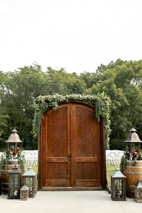 Enchanting outdoor wedding entrance to ceremony with beautiful fall florals and lanterns surrounding gorgeous wooden doors. Wedding Doors Outside Outdoor Ceremony, Outdoor Ceremony Entrance Ideas, Outdoor Ceremony Entrance, Wedding Door Entrance Outside, Outdoor Wedding With Doors Entrance, Wedding Outdoor Doors, Wedding Entrance Outdoor Ceremony, Wedding Ceremony Doors Entrance, Outdoor Wedding Bride Entrance